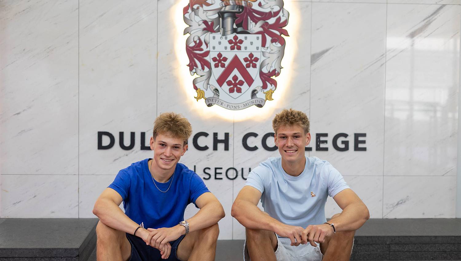 Anton V and Edgar V sitting together in front of the Dulwich College Seoul crest.