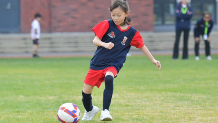 A Junior School student in the Borussia Football CCA kicks the ball on the school field.
